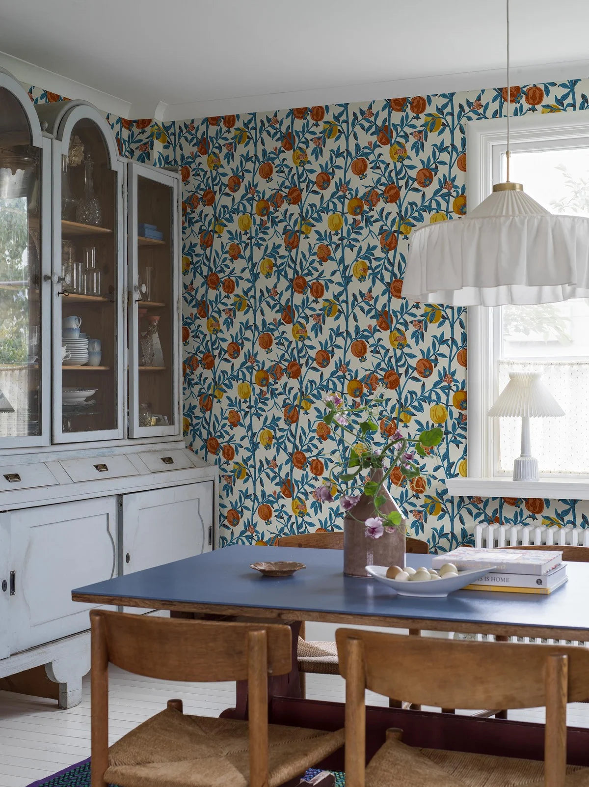 Wallpaper with a botanical pattern of pomegranates in white with blue and orange