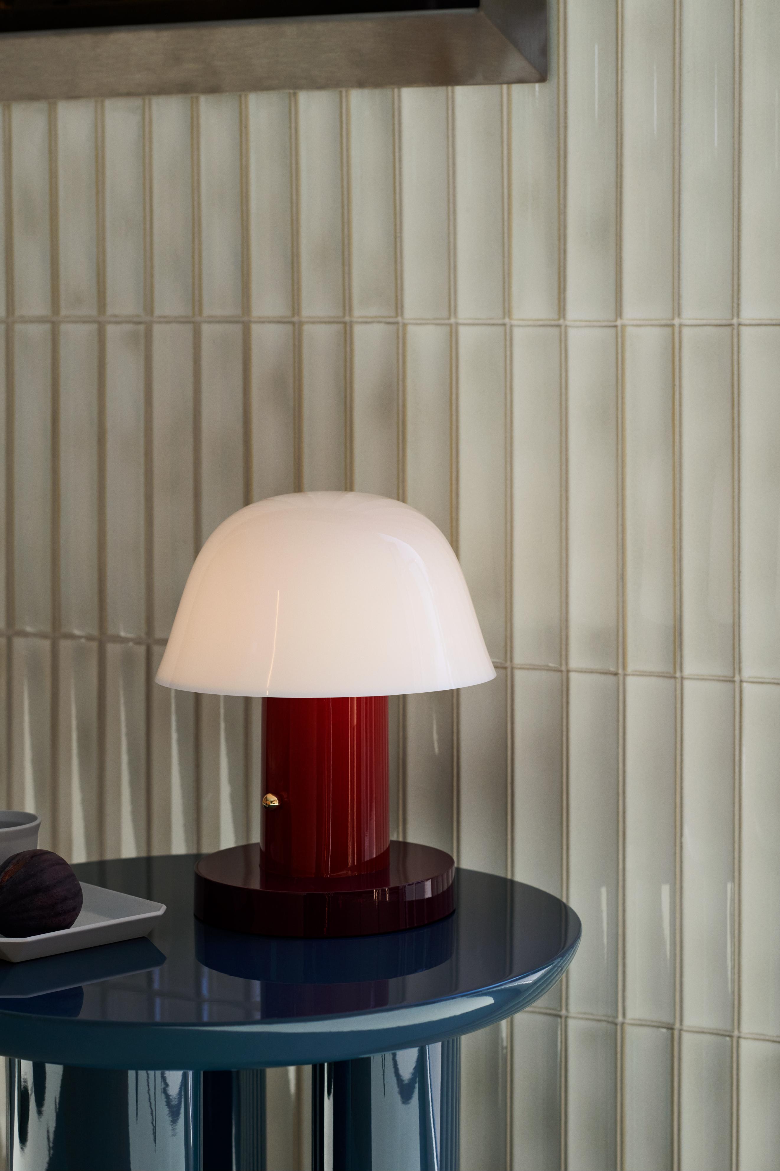 Draagbare lamp SETAGO JH27 met een crèmekleurige kap en een donkerrode voet.
